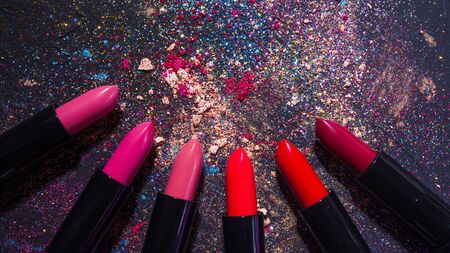 Cosmetics and beauty industry, a set of lipsticks on a background of loose powder and eye shadow, dark textured backgroundの写真素材
