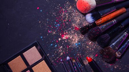 Cosmetics and beauty, still life with a palette of shadows, makeup brushes and a set of lipsticks, dark textured backgroundの写真素材
