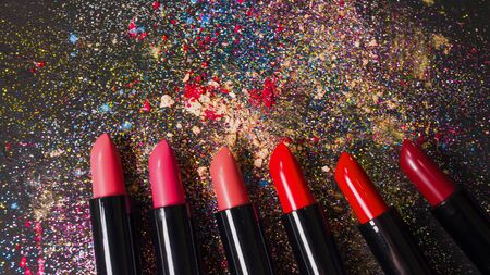 Cosmetics and beauty industry, a set of lipsticks on a background of loose powder and eye shadow, dark textured backgroundの写真素材