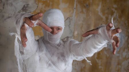Halloween image, mummy in bandages, risen dead legendary character. young woman in the form of a mummy wrapped in bandages, against the textured old wallの写真素材