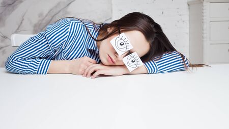Drowsiness and procrastination. A student pretends to work, a girl in glasses with stickers with a pattern of open eyesの写真素材
