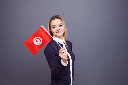 Immigration and the study of foreign languages, concept. A young smiling woman with a Tunisia flag in her hand. Girl waving a Tunisia flag on a gray backgroundの写真素材