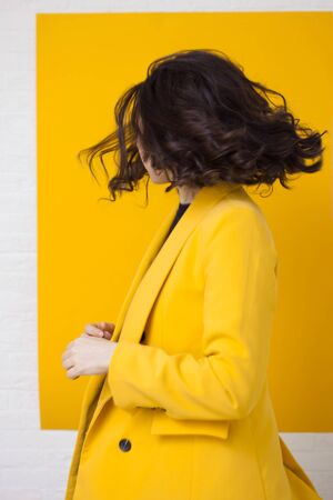 Stylish young woman in a yellow jacket on a yellow background, happy and dancing. Background with white frameの写真素材