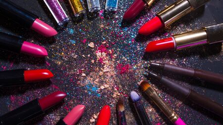 Cosmetics and beauty industry, a set of lipsticks on a background of loose powder and eye shadow, dark textured background with copy space in the centerの写真素材