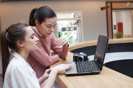 photographer or blogger instructs an Intern or discusses a joint project with a colleague. Two young women look at one laptop and discuss the topicの写真素材