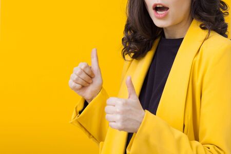 Young positive woman in yellow, bright portrait on a yellow background. Funny girl dancing, shows two hands thumbs up, class superの写真素材