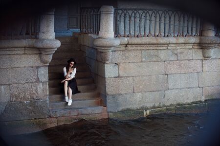 young woman in a hat and with a backpack walks in the city and uses a smartphone. Hipster on a walk uses the phone and takes photos for social networksの写真素材