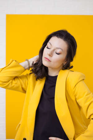 Stylish young woman in a yellow jacket on a yellow background, bright and trendy portraitの写真素材