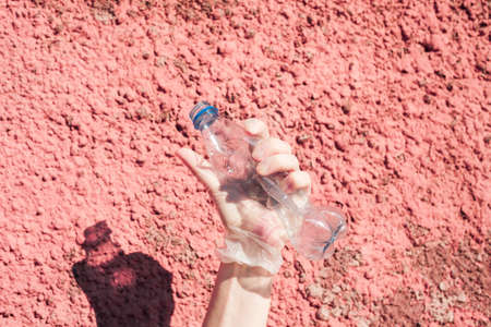 We are against plastic garbage. A hand in protective gloves clutches an empty disposable bottle....