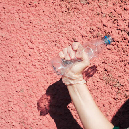 We are against plastic garbage. A hand in protective gloves clutches an empty disposable bottle. Separation of waste, recycling of plastics, the conceptの写真素材