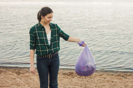 Taking care of our planet, fighting plastic garbage in nature. A young female volunteer finished cleaning the beachの写真素材