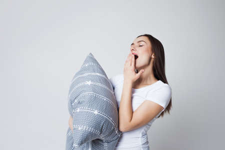 Sleep and drowsiness, girl grabs a pillow and yawns. young woman got up in the morning but still wants to sleepの写真素材