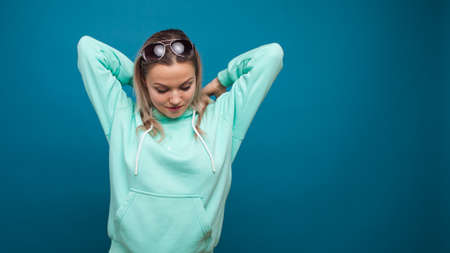 Cheerful hipster girl in hoodie and sunglasses. young woman in the youth outfit portrait on a blue background.の写真素材