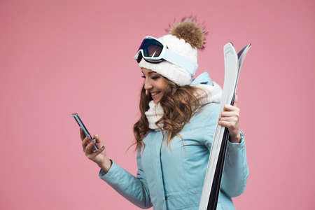 young woman with skis uses a smartphone to plan her ski runs. Winter holidays at a ski resort. Girl...