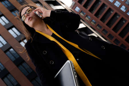 young specialist with a laptop and smartphone in hand, hurrying to work. A young woman in a coat and...