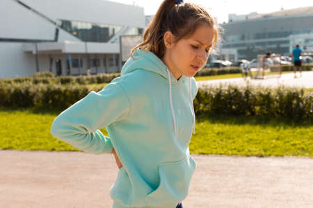 Sports injuries, a young female athlete kneads the lower back, sprains or muscles. The runner in the...