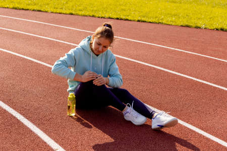 Sports injuries, a young female athlete kneads her knee, sprains or muscles. Runner in a blue hoodie...