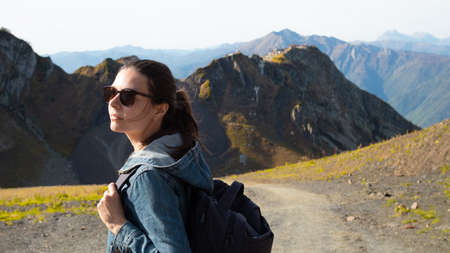 Hiking in the mountains, a young female tourist with a backpack is walking along a path in the...