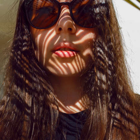 Young female tourist in sunglasses, summer by the sea. portrait under a palm tree, shadow on the...