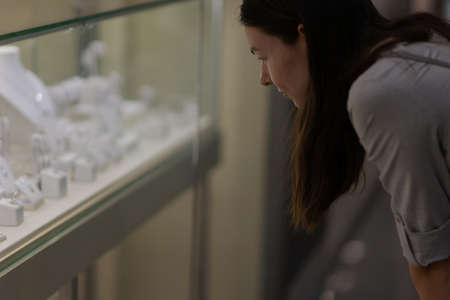 A young woman in a store admires a display of jewelry with diamonds and precious stones. Jewelry...