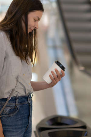 Sorting garbage in public places. A young woman chooses where to throw a disposable Cup of coffee. close upの写真素材