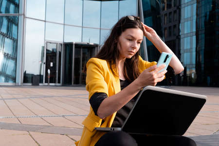 freelancer with a laptop is sitting on the stairs near the business center, a young woman in a...