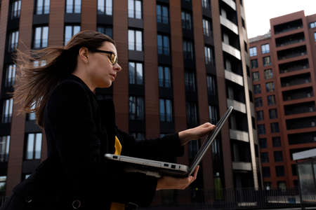 young woman in a coat looks at an open laptop, a portrait of a business woman against the background...