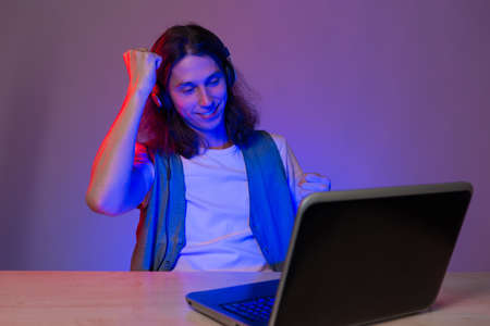 Student or gamer at a laptop, portrait in neon tinting. Funny guy geek writes code.の写真素材