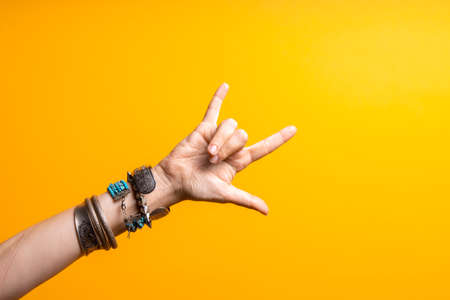 Hand gestures. Thumbs up, thats a cool gesture of the rocker. womens hand with lots of bracelets, youth fun style. bright yellow backgroundの写真素材