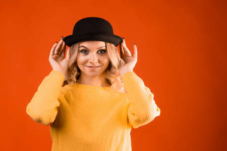 Stylish young woman in knitted clothes and bowler hat, bright orange background, studio portrait, copy spaceの写真素材