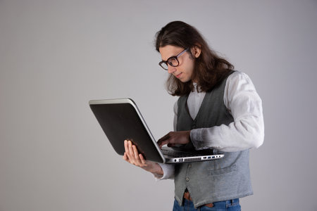 Programming and writing code, developing software products. Geek guy, with long hair and glasses, holding a laptop, gray backgroundの写真素材
