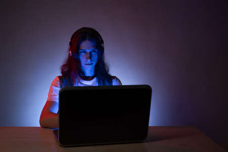 Student or programmer at a laptop, portrait in neon tinting. Funny guy geek writes code. Training in digital specialties, website development, design and programming.の写真素材