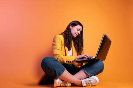 freelancer at a laptop, a young specialist working remotely. A young woman in modern-style clothing holds a laptop on her lap and types text, business correspondence, or programming.の写真素材