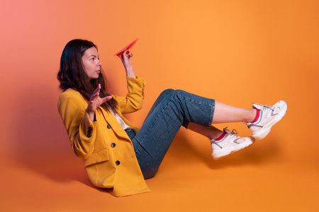Launch a paper airplane, a startup concept. Young brunette woman in yellow sitting on a yellow...