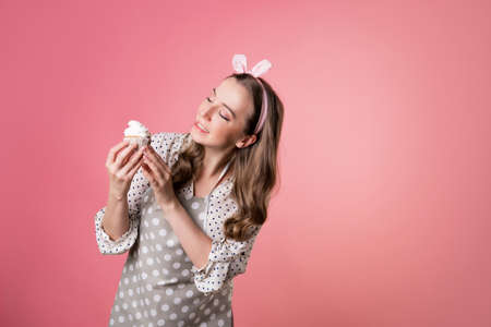young charming female pastry chef tastes a muffin with cream. A cook in a polka-dot apron.