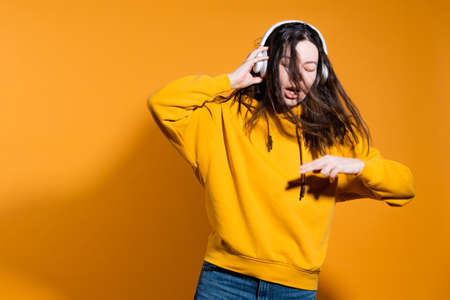 Happy dancing music lover. A young woman in a yellow hoodie with white wireless headphones,の写真素材