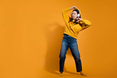 Happy dancing music lover. A young woman in a yellow hoodie with white wireless headphones,の写真素材