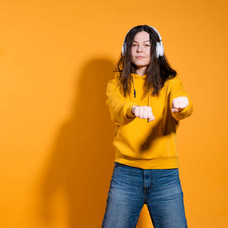 Happy dancing music lover. A young woman in a yellow hoodie with white wireless headphones,