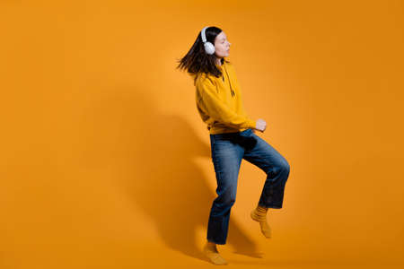 Happy dancing music lover. A young woman in a yellow hoodie with white wireless headphones,の写真素材