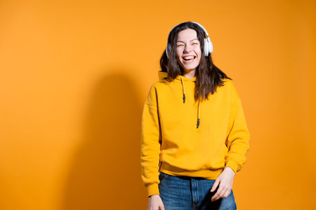Happy dancing music lover. A young woman in a yellow hoodie with white wireless headphones,の写真素材