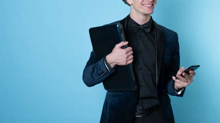 young business man in a suit uses a smartphone and holds a laptop in his hands,