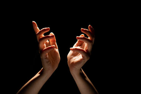 Beautiful folded hands with light on top, black background. Prayer or creating a miracle.