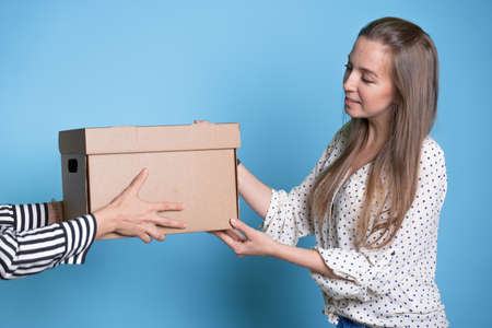 You send, transfer and accept a box with a parcel from hand to hand, a young woman receives a gift or delivery.の写真素材