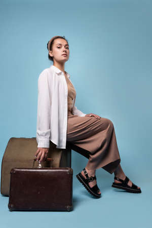 young woman in summer pants and a white shirt is sitting on vintage leather suitcasesの写真素材