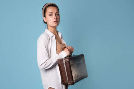 A young brunette in a white shirt stands grabbing her luggage. The traveler is worried before the flight,の写真素材