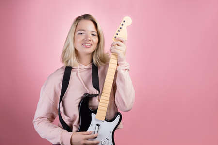 A young charming blonde is laughing and playing a toy electric guitar, fun and hobby.
