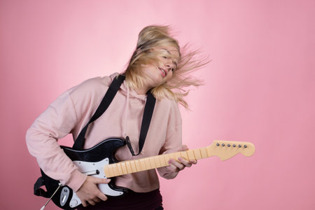 A young charming blonde is laughing and playing a toy electric guitar, fun and hobby.の写真素材