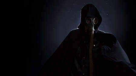 A gloomy man in dark clothes, a black hood on his head, a gas mask protects his face.の写真素材