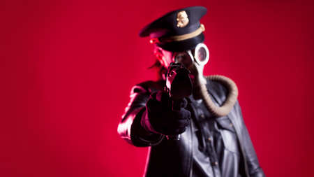 fantastic Nazi in black leather clothes and a cap with a gas mask on face with a gun in his hand, red backgroundの写真素材