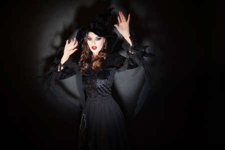 witch at Halloween party, a young beautiful brunette woman in a classic witch costume with a pointed hat. Caught off guard in the spotlight, a witch is discovered.の写真素材